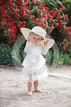 Little girl in rose garden next to a big bush of red roses