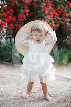 Little girl in rose garden next to a big bush of red roses