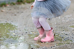 Little girl in rubber boots and tutu dress jumping in puddle. Water is splashing from kid feet as she is jumping and playing in