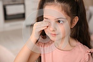 Little girl rubbing eye at home.