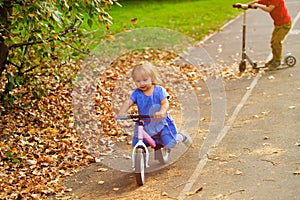 Little girl on runbike and boy at scooter in autumn, kids sport