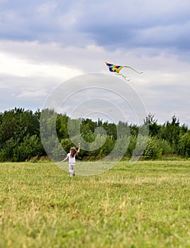 A little girl running on green grass after the bright flying kite