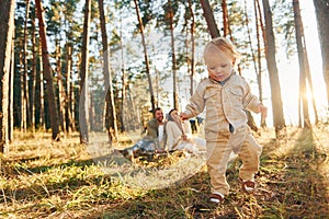 Little girl is running. Happy family of father, mother and little daughter is in the forest