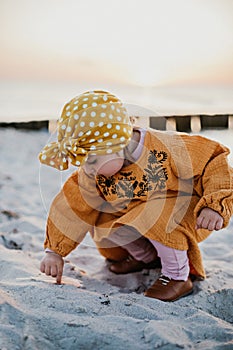 Little girl running her finger along the sand on the beach during sunset