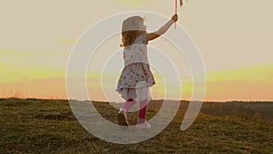 Little Girl Running On Nature At Sunset. Girl Holding Toy Windmill Moving In The Wind.