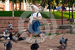 Little girl running near doves, chasing pigeons, happy child with smiling face. Kid is feeding pigeons in city park