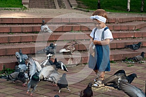 Little girl running near doves, chasing pigeons, happy child with smiling face. Kid is feeding pigeons in city park