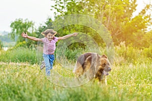 Little girl running after a shepherd dog on the meadow