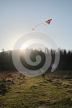 Little girl runs across field on green grass at sunset and launches multicolored kite into sky. Have fun spending childhood