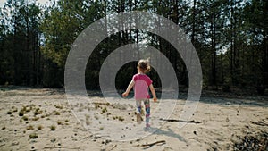 Little girl runs across the sand in a forest