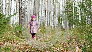 A little girl runs along a path in a birch forest.