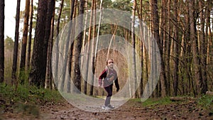 The little girl runs along the path road in the pine forest. Dressed in the leather jacket.