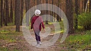 The little girl runs along the path road in the pine forest. Dressed in the leather jacket.