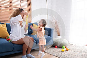 A little girl runs and plays with a small soap bubble that his mother blows for him to play with. In the living room