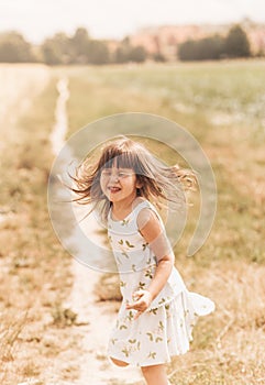 A little girl runs through a wheat field. The girl has fun and laughs with delight. Field with ripe ears of corn at sunset