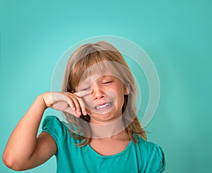 Little girl with sad expression and tears. Crying child on turquoise background. Emotions.