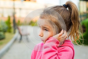 A little girl with a sad and frightened face holds her cheek with her hand - a tooth hurts. Ear pain, toothache, swollen cheek and