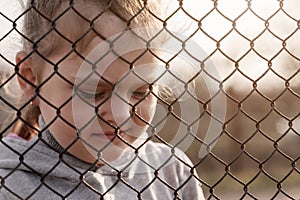Little girl with a sad look behind a metal fence, social problems, raising children in orphanages photo