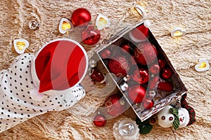 Little girl in Santa Claus red hat is playing with Christmas decorations and Christmas lights on a beige plaid, top view.