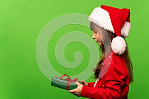 A little girl in a Santa hat holds a Christmas present in her hand, looks and will open it.