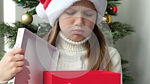 Little girl in Santa hat opening Christmas gift and gets upset