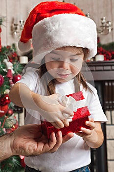 Little girl in Santa hat opens red gift box for Christmas in fat