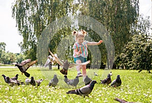 Little girl scares pigeons fun game summer. ecology, runs on the grass in the city park outdoors, lifestyle