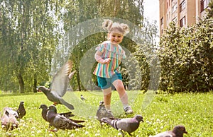 Little girl scares pigeons fun game summer. ecology, runs on the grass in the city park outdoors, lifestyle