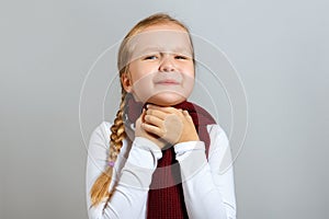 A little girl in a scarf suffers from a sore throat. The child holds on to the neck. The concept of the season of colds