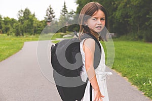 Little girl with school backpack on path looking back to camera