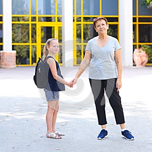 Little girl with school bag or satchel walking to school with grandmother.