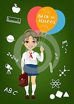 Little girl in school uniform holding balloons with back to school text standing in front of school items on blackboard