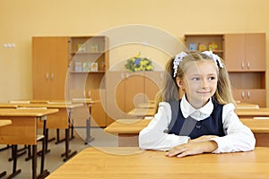 Little girl in school uniform sits at school desk