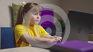 Little girl schooler does homework on laptop at desk in room