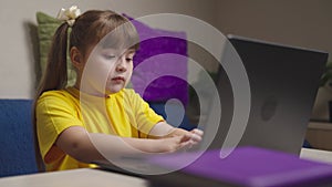 Little girl schooler does homework on laptop at desk in room