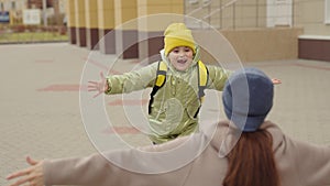 little girl schoolgirl with backpack runs hug her mother, kid rejoice over lessons, happy family, school bag behind back