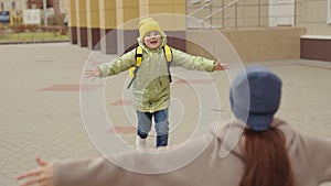 little girl schoolgirl with backpack runs hug her mother, kid rejoice over lessons, happy family, school bag behind back