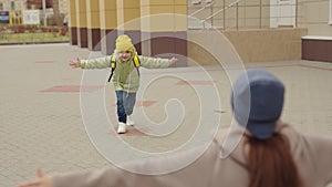 little girl schoolgirl with backpack runs hug her mother, kid rejoice over lessons, happy family, school bag behind back