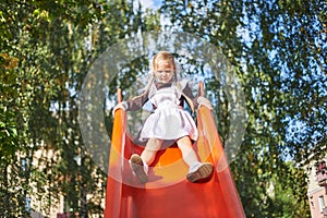 little girl schoolgirl plays in uniform in the yard. The child rolls from the children& x27;s slide on the playground.