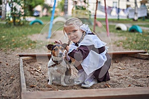 Little girl schoolgirl in uniform hugs a little dog in the yard.