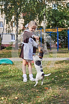 little girl schoolgirl in uniform trains a dog in the yard.