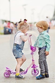 Little girl with scooter and little boy stand on