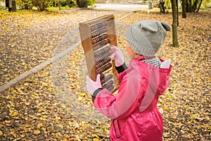 Little girl scores on old mechanical abacus in the autumn park. A child learns to count numbers on a retro calculator. Teaching a