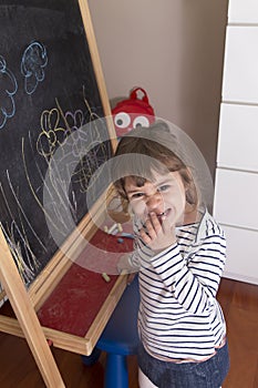 Little girl scribbling on drawing of flowers on blackboard