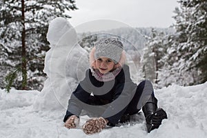 Little girl sculpts snowman in winter snowy Park.