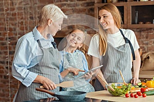 Little girl showing granny and mom recipes on digital tablet