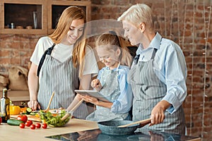 Little girl showing mom and granny new recipes on tablet