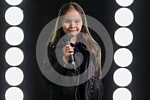 Little girl singing in front of stage lights