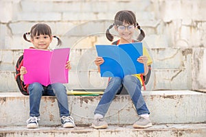 Little Girl and sister reading a book together. Adorable Asian kids enjoying studying outdoors togther. Education photo