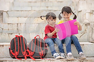 Little Girl and sister reading a book together. Adorable Asian kids enjoying studying outdoors togther. Education photo